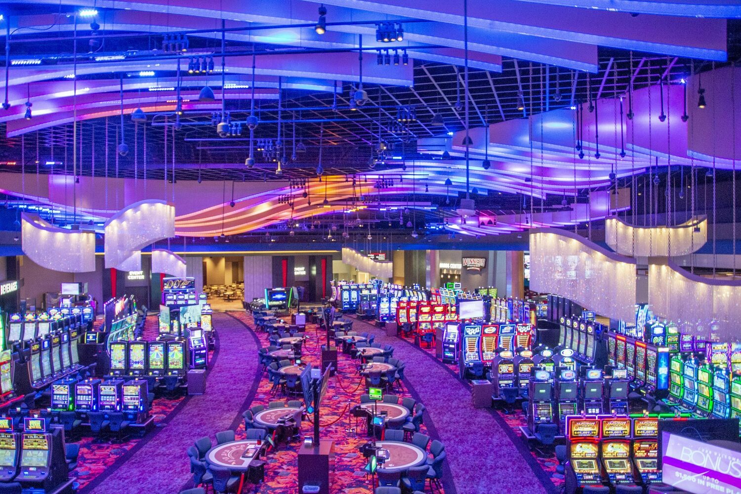 An elevated wide view of West Valley’s table games and rows of slots beneath blue illuminated ceiling fins