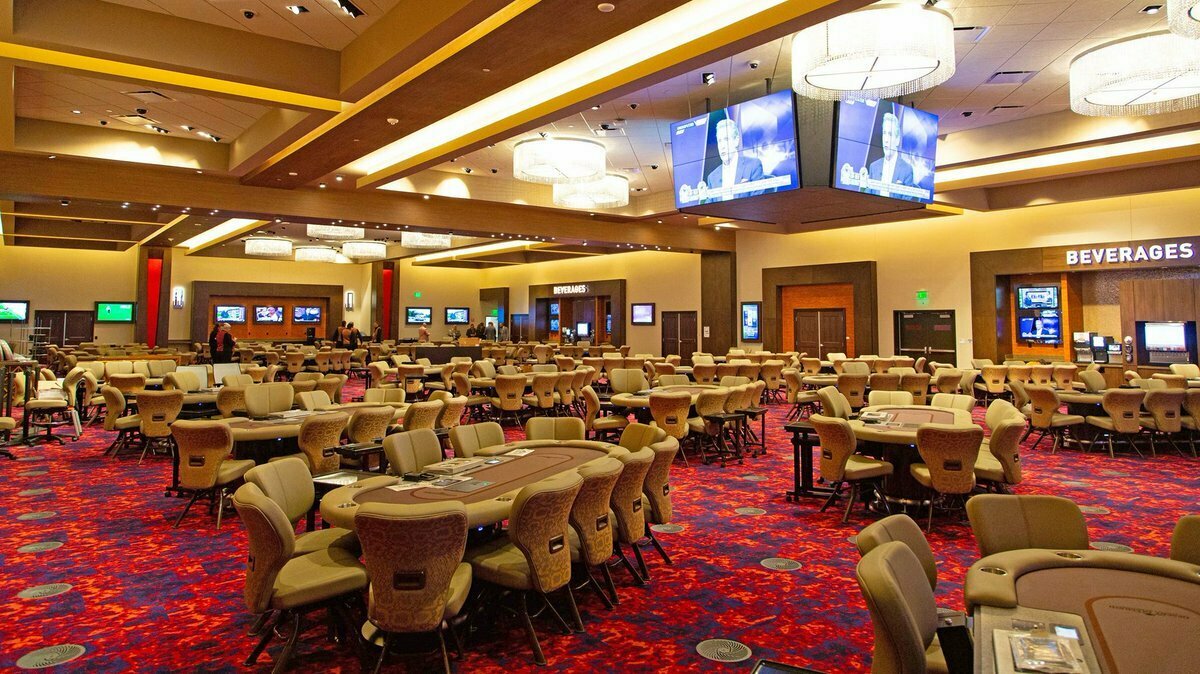 A wide view across the dedicated West Valley poker room with its many tables, upholstered chairs and gold ceiling
